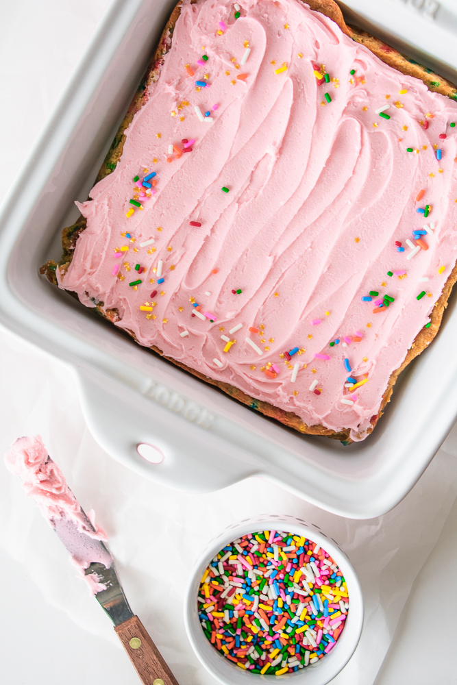 Blondies in a pan with pink frosting and sprinkles