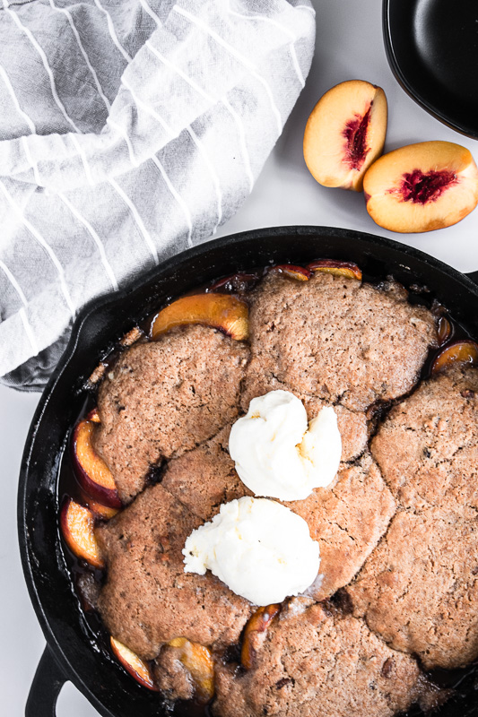 Peach cobbler with vanilla bean ice cream on top in a cast iron skillet.