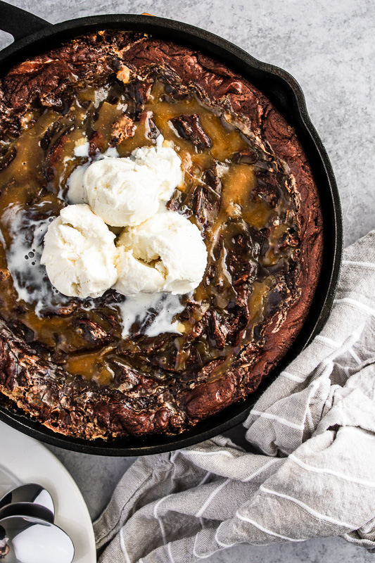 Skillet brownie with salted caramel sauce swirled throughout and vanilla bean ice cream on top