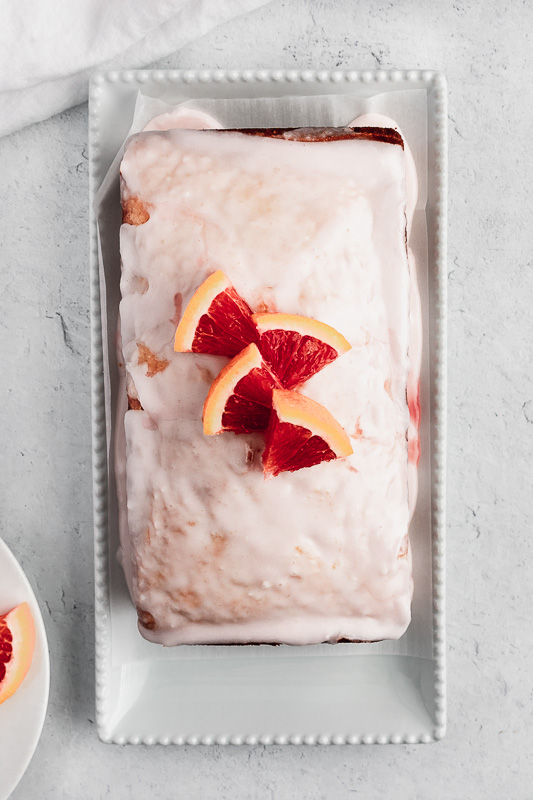 Blood orange loaf cake on a white platter with blood orange glaze