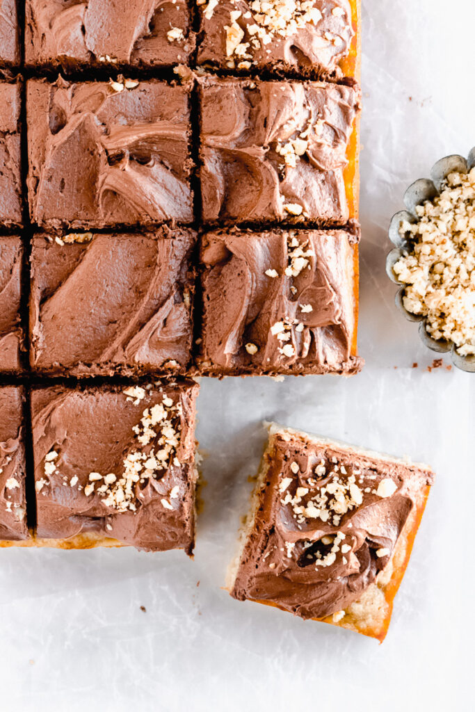 Slices of banana snack cake with dark chocolate buttercream and pecans sprinkled on top