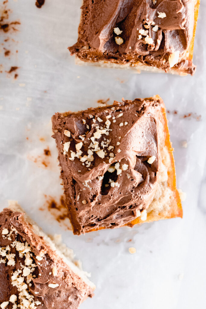 Slices of banana snack cake with dark chocolate buttercream and pecans sprinkled on top