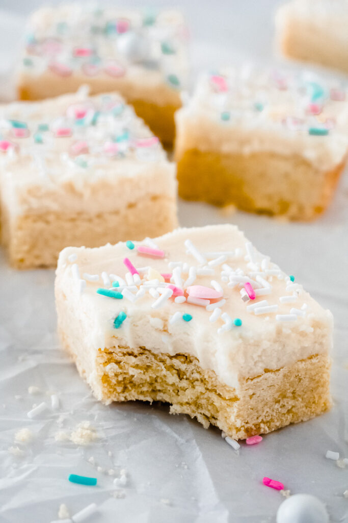 A bite taken out of a lemon sugar cookie bar topped with vanilla cream cheese buttercream and spring colored sprinkles