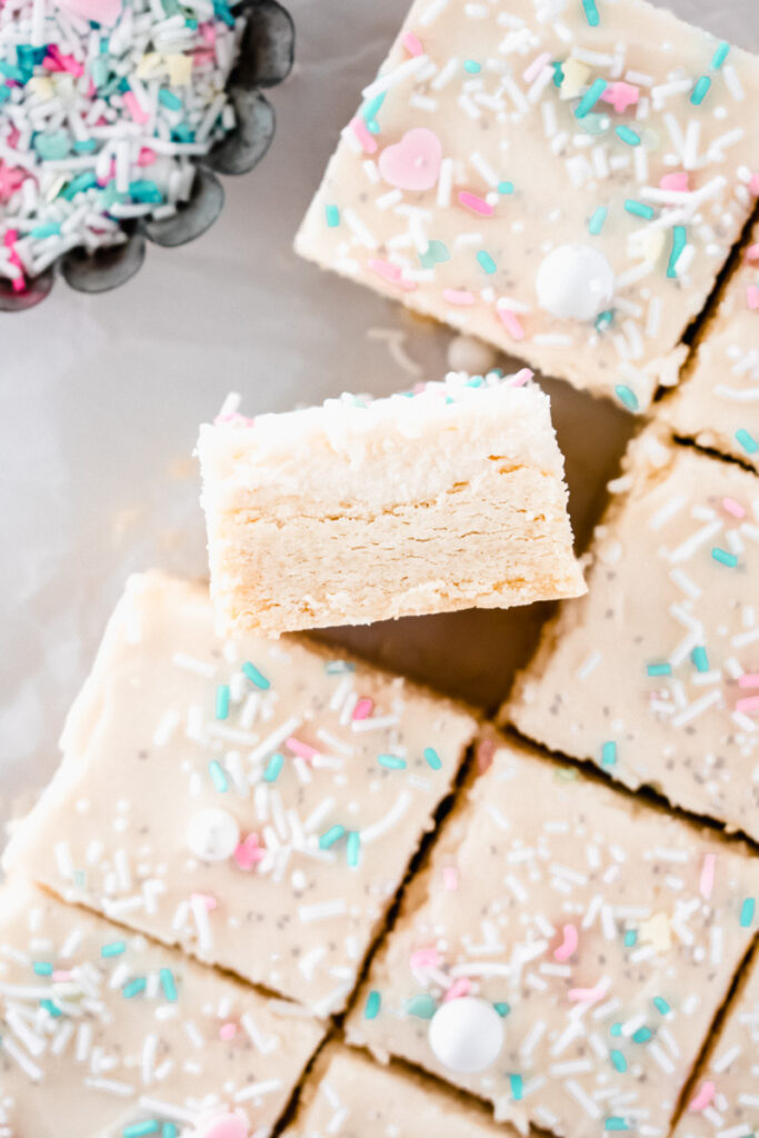 Lemon sugar cookie bar on its side on white parchment paper with sprinkles in the background
